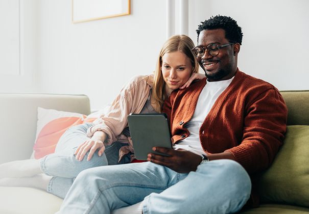 Couple souriant en consultant une tablette ensemble sur un divan