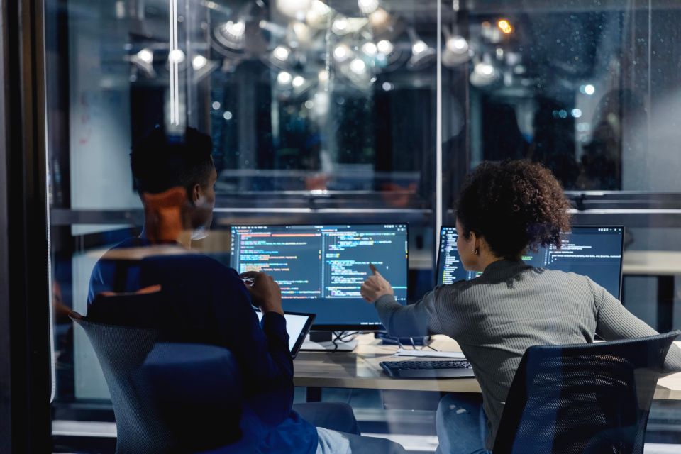 Deux employés sont assis à un bureau et examinent du code à l’écran d’un ordinateur.