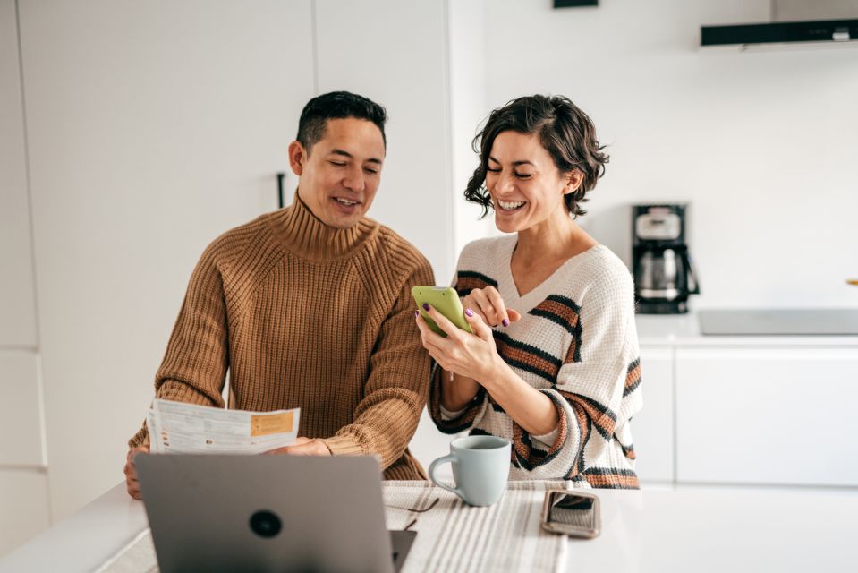 Couple dans la cuisine avec des factures tout en faisant des opérations bancaires en ligne