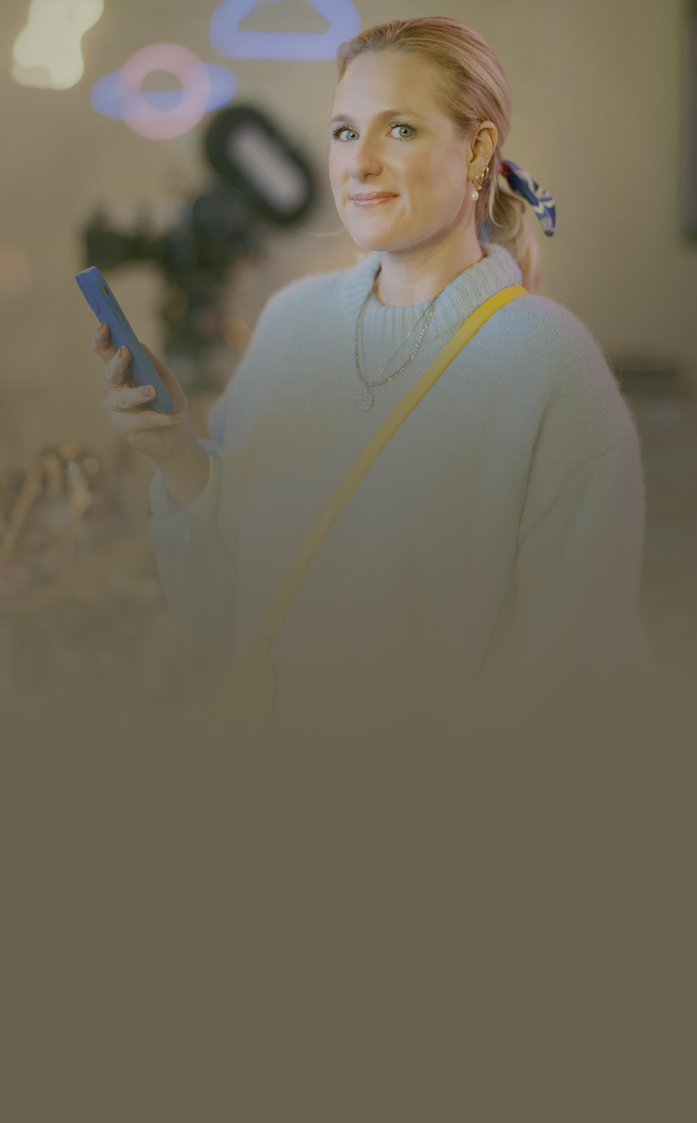 Femme souriant à la caméra, un téléphone cellulaire dans la main